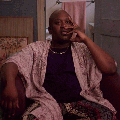 A Man Wearing A Purple Shirt And A White Robe Sits In A Chair With His Hand On His Face GIF