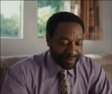A Man Wearing A Purple Shirt And Tie Is Sitting On A Couch . GIF