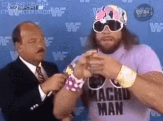 A Man Wearing A Purple Shirt That Says Macho Man Is Standing Next To A Man In A Suit And Tie . GIF