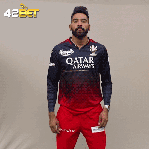 A Man Wearing A Qatar Airways Jersey Stands In Front Of A 42Bet Banner GIF