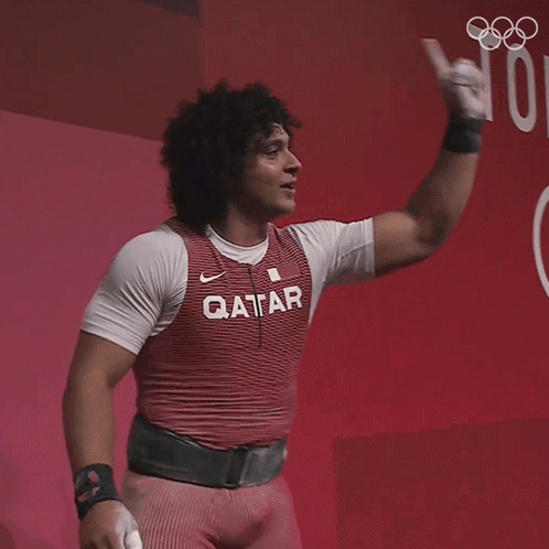 A Man Wearing A Qatar Shirt Holds His Fist Up GIF