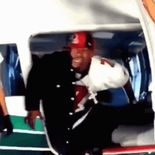 A Man Wearing A Red And Black Hat Is Getting Out Of A Helicopter GIF