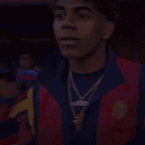 a man wearing a red and blue jacket with a gold necklace around his neck