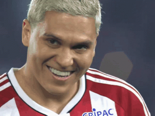 a man wearing a red and white jersey that says gripac smiles