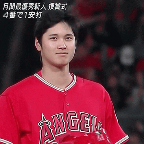A Man Wearing A Red Angels Jersey Stands In Front Of A Crowd GIF