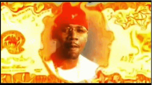 A Man Wearing A Red Beanie And Glasses Is Standing In Front Of A Fire . GIF