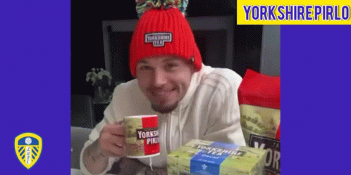 A Man Wearing A Red Beanie Is Holding A Yorkshire Pirlo Cup GIF