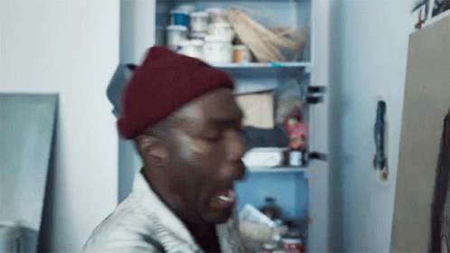 A Man Wearing A Red Beanie Is Standing In Front Of A Refrigerator . GIF