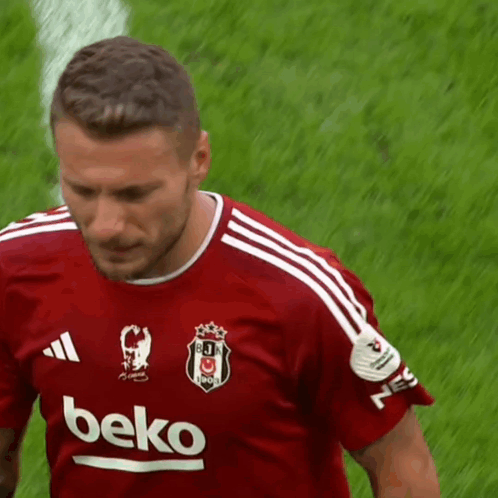 A Man Wearing A Red Beko Shirt Stands On A Field GIF