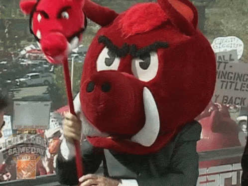 A Man Wearing A Red Boar Mascot Costume Holds A Red Stick In Front Of An Espn Sign GIF