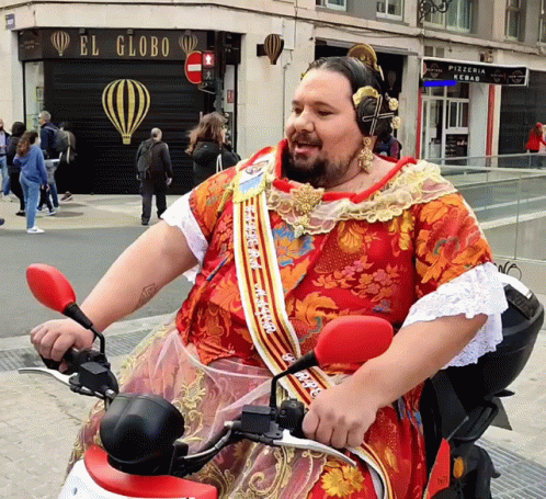 A Man Wearing A Red Dress Is Riding A Motorcycle In Front Of A Store Called El Globo GIF