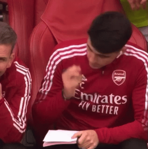 A Man Wearing A Red Emirates Fly Better Jersey Is Sitting In A Stadium . GIF