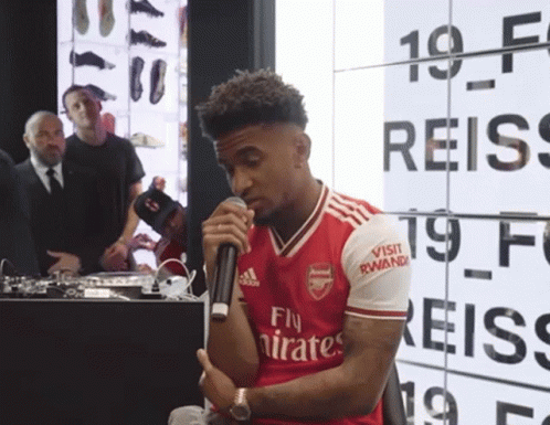 A Man Wearing A Red Fly Emirates Jersey Holds A Microphone GIF