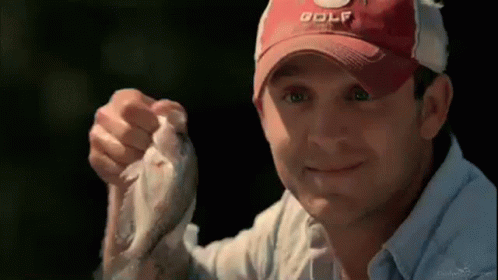 A Man Wearing A Red Golf Hat Is Holding A Small Fish In His Hand . GIF