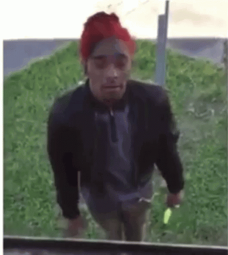 A Man Wearing A Red Hat And A Black Jacket Is Walking In The Grass . GIF
