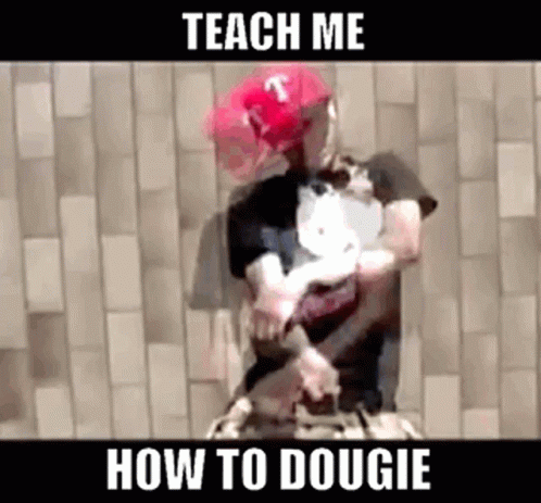 A Man Wearing A Red Hat And A Black Shirt Is Holding A Dog While Standing In Front Of A Brick Wall . GIF