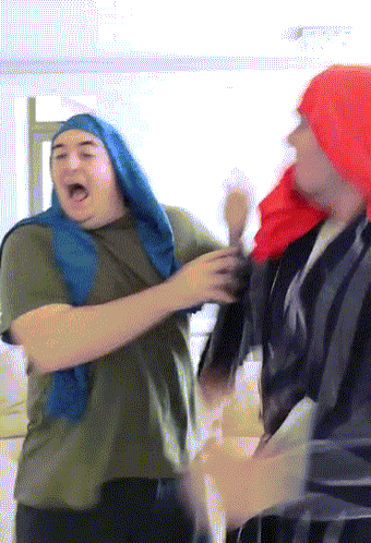 A Man Wearing A Red Hat And A Blue Scarf Stands Next To Another Man GIF