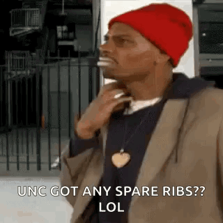 A Man Wearing A Red Hat And A Brown Jacket Is Standing In Front Of A Fence And Talking On A Cell Phone . GIF