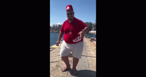 A Man Wearing A Red Hat And A Red Shirt Is Standing On A Pier . GIF