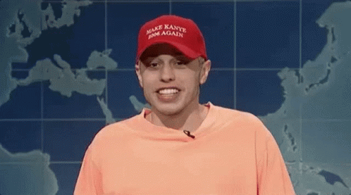 a man wearing a red hat and an orange shirt is smiling in front of a map of the world .