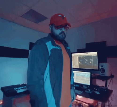 A Man Wearing A Red Hat And Sunglasses Is Standing In Front Of A Computer Monitor GIF