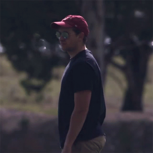 A Man Wearing A Red Hat And Sunglasses Stands In A Field GIF