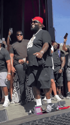 A Man Wearing A Red Hat And Sunglasses Stands In Front Of A Crowd Of People GIF
