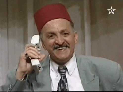 A Man Wearing A Red Hat And Tie Is Talking On A Cell Phone . GIF