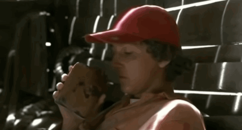 A Man Wearing A Red Hat Is Drinking From A Brown Cup GIF