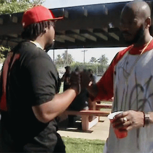 A Man Wearing A Red Hat Is Shaking Hands With Another Man Wearing A White Shirt With Graffiti On It GIF