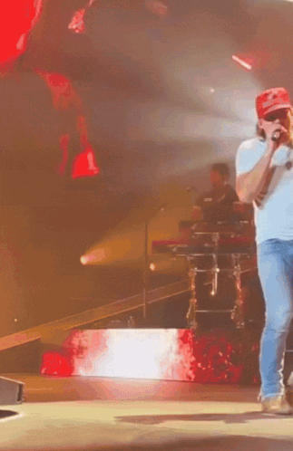 A Man Wearing A Red Hat That Says Supreme On It Is Singing Into A Microphone On A Stage GIF