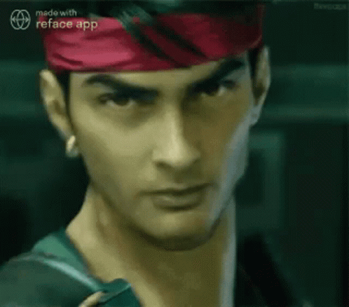 A Man Wearing A Red Headband And A Green Jacket Is Looking At The Camera . GIF