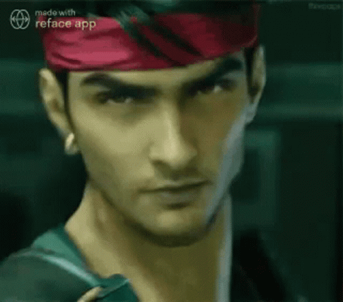 A Man Wearing A Red Headband And A Green Shirt Is Looking At The Camera . GIF