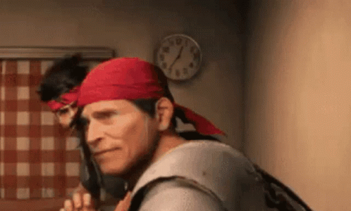 A Man Wearing A Red Headband Is Standing In Front Of A Clock That Shows The Time As 7:15 GIF