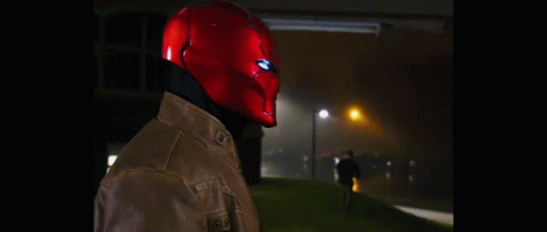 A Man Wearing A Red Helmet And A Leather Jacket Is Standing In The Dark . GIF