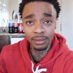 A Man Wearing A Red Hoodie Is Looking At The Camera . GIF