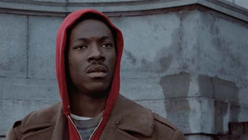 A Man Wearing A Red Hoodie Is Standing In Front Of A Building GIF