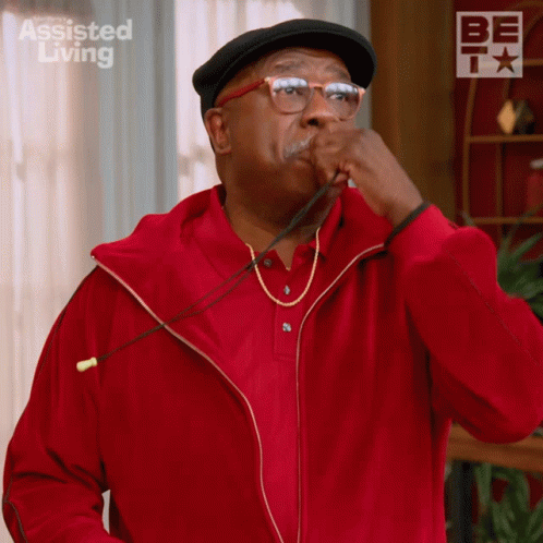 A Man Wearing A Red Jacket And A Black Hat With Assisted Living On The Bottom Right GIF