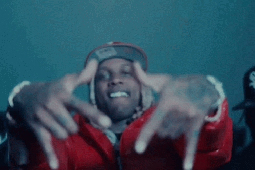 A Man Wearing A Red Jacket And A Hat Is Making A Hand Gesture . GIF