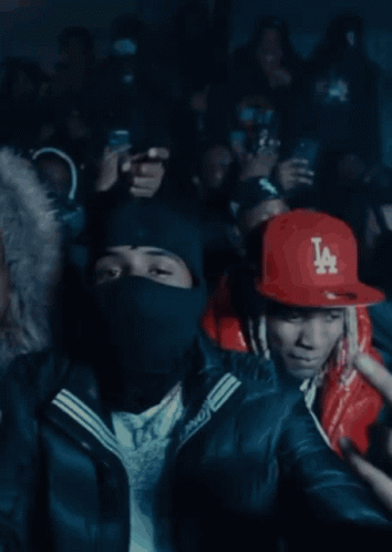 A Man Wearing A Red Jacket And A La Hat Stands In Front Of A Crowd GIF