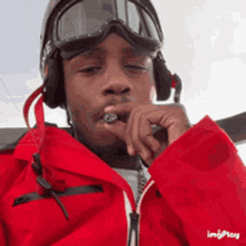 A Man Wearing A Red Jacket , Goggles And Headphones Is Smoking A Cigarette . GIF