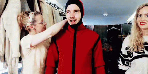 A Man Wearing A Red Jacket With A Hood Is Being Helped By Two Women . GIF