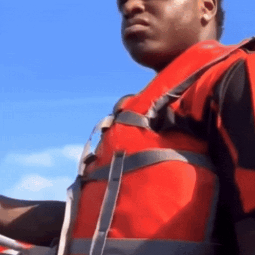A Man Wearing A Red Life Jacket Is Holding A Steering Wheel GIF