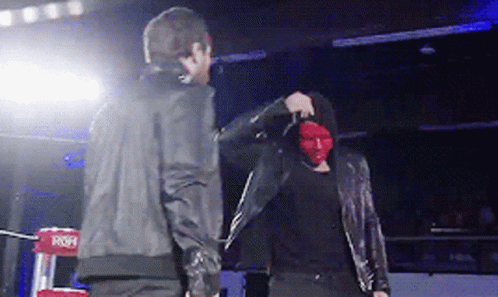 A Man Wearing A Red Mask Stands Next To Another Man In A Black Jacket GIF