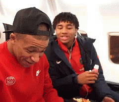 a man wearing a red nike shirt is sitting next to another man wearing a black hat .