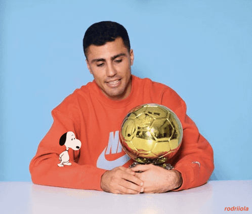 A Man Wearing A Red Nike Sweatshirt Is Holding A Golden Soccer Ball GIF