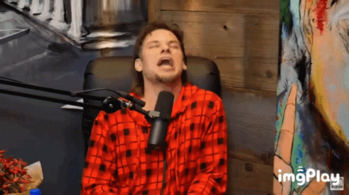 A Man Wearing A Red Plaid Shirt Is Sitting In Front Of A Microphone With His Eyes Closed And The Word Imgplay Below Him GIF