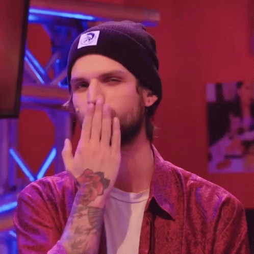 A Man Wearing A Red Shirt And A Black Beanie Is Covering His Mouth GIF