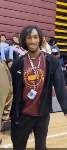 a man wearing a red shirt and a black jacket is standing on a basketball court with his arms outstretched .