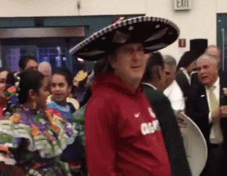 A Man Wearing A Red Shirt And A Sombrero Is Standing In A Crowd . GIF